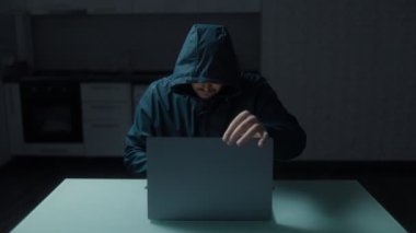 Kimliği belirsiz bir adam mutfakta dizüstü bilgisayarla oturuyor. Görüntü, siber aktiviteleri ima ederek odaklanmış bir çalışma anını yakalar.