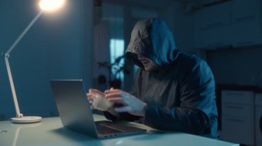 Stresli bir hacker evdeki karanlıkta dizüstü bilgisayarda hızla yazarak başarısızlığından duyduğu hayal kırıklığını ve öfkeyi gösteriyor. Loş ışık yoğun odaklanmasını vurguluyor..