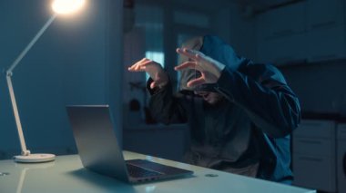 Erkek bir hacker evdeki karanlık bir odada dizüstü bilgisayarda çalışıyor, uzaktan kumandalı dolandırıcılığa odaklanıyor, gizlilik ve siber aktivite ortamı yaratıyor..