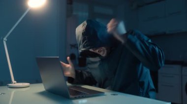 Hüsrana uğramış bir hacker karanlık ev ortamında başarısız bir denemeden sonra öfkesini ve stresini ifade etmek için loş bir odada dizüstü bilgisayarıyla bir masada oturuyor..