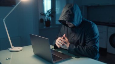 Loş bir odada dizüstü bilgisayarı üzerinde çalışan gizemli bir erkek hacker portresi. Karanlık çevre ve parlayan ekran ciddi ve gizli bir ruh hali oluşturuyordu..