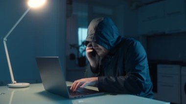 Bilgisayarda siber suçlu daktilo kullanıyor, karanlık bir odada dolandırıcılık yapıyor. Hacker, başarılı veri sızıntısını kutluyor. Neşe ve beceri karışımı bir şey sergiliyor..