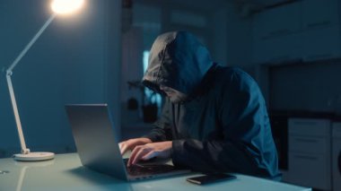 Başarılı bir hacker başarısından zevk alır, masada dizüstü bilgisayarda yazarak. Karanlık oda ve ev dekorasyonu dijital zaferine odaklanıyor..