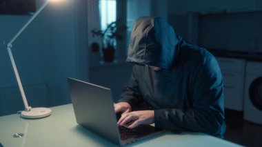 Karanlık bir ofisteki bir bilgisayar korsanı dizüstü bilgisayarında hızlı bir şekilde siber suçlar ve veri sızıntılarıyla ilişkili anonimliği ve gizliliği simgeliyor..
