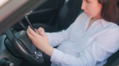 Arabada hamile bir kadın, sürücü koltuğunda rahatlarken ve akıllı telefonuyla internette sörf yaparken huzurlu ve odaklanmış bir ifadeyle..