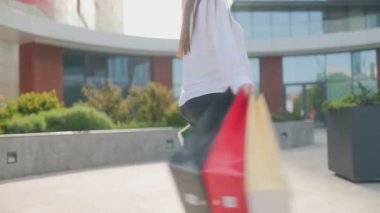 Genç bir anne şehir dışında şık bir günün ardından kendinden emin bir şekilde renkli alışveriş torbalarıyla hava atıyor..