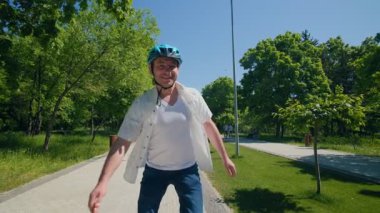 Genç bir adam heyecanla kollarını kaldırarak tekere güvenle biniyor. Etrafında güneşin ve doğanın tadını çıkarırken canlı bir parkta yeteneklerini sergiliyor..