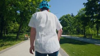 Genç bir adam yüksek teknolojili bir tekerle ağaçlarla kaplı bir şehir parkında geziyor, güneşli bir günde dengenin, pürüzsüz hızın ve doğal manzaranın tadını çıkarıyor..