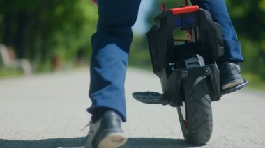 Sıradan giyimli bir adam, tek tekerli bir tekerin üzerinde, parlak, açık bir park alanında süzülür. Teknolojik olarak, gidip gelme tarzını gösterir..