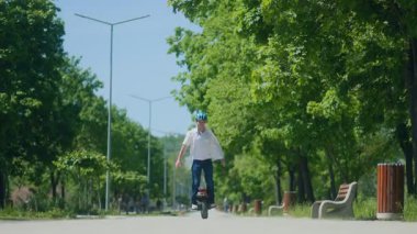 Omuzlarında güneş ışığıyla, genç bir adam elektrikli bir tek tekerlekli bisikletle parkta sorunsuzca süzülüyor. Sakin, kendine güvenen bir sabah yolculuğu.