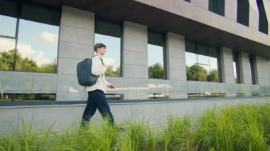 Bir lise öğrencisi omuzlarında sırt çantasıyla sınıfa doğru tırmanıyor. Modern bina ve güneş ışığı bir okul gününün başlangıcını vurguluyor.