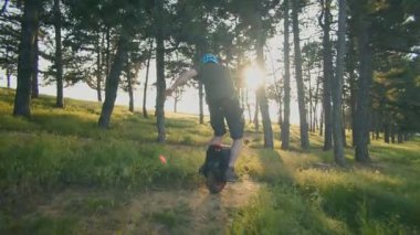 Bir adam altın saatinde ormanda tek tekerlekli bisiklete biner. Kask takıyor, ağaçlar ve yumuşak güneş ışığıyla çevrili gezintiden zevk alıyor..