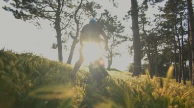 Ağaçların arasında güneş parlayan ağaçlık bir patika boyunca elektrikli tek tekerlekli bisikletine binen bir adam. Kask takıyor ve her dönemeci seviyor..
