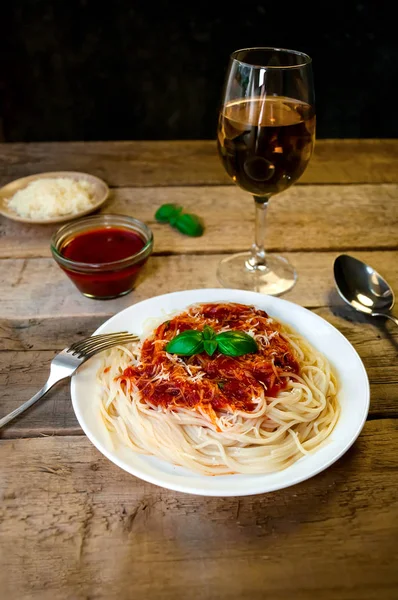 Makaron spaghetti z sosem pomidorowym, Sery żółte i bazylii z kieliszek do wina na drewnianym stole. Tradycyjne dania kuchni włoskiej — Zdjęcie stockowe