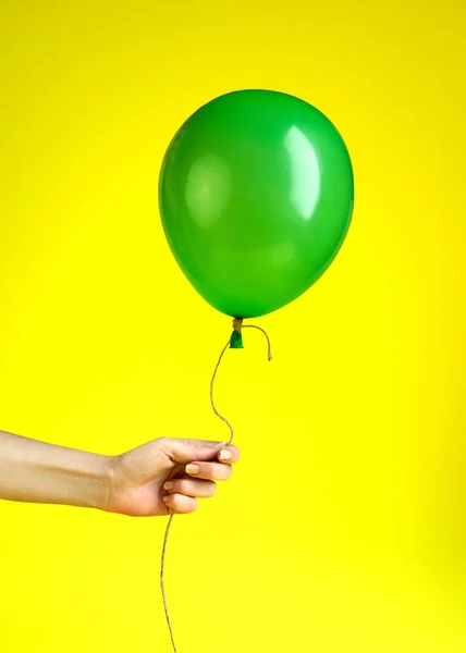 Vrouw houdt in Hand een groene ballon op gele achtergrond — Stockfoto