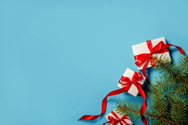 Kerstcadeaus witte doos met rood lint op blauwe achtergrond Fir boomtakken op blauwe achtergrond plat lag kopie ruimte — Stockfoto