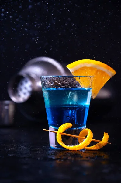 Tiros com Rum Branco, Licor Azul Curaçao e Fatia de Laranja. Cocktail de camada alcoólica com agitador em movimento de congelamento, gotas em respingo líquido em fundo escuro — Fotografia de Stock