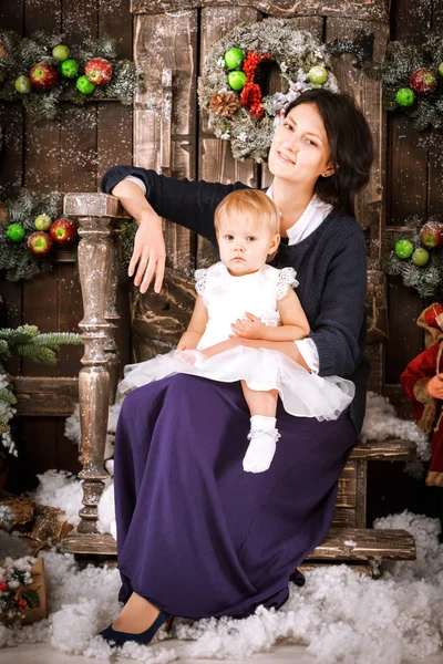 Feliz madre sostiene hija niña en sus vueltas cerca del árbol de Navidad en el interior de estilo loft de madera marrón — Foto de Stock