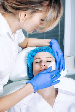 Kozmetik uzmanı hastaların yüzüne anestezi ile krem sürüyor. Cilt biyo-evyalizasyon işlemi için hazırlanıyor