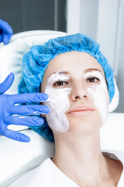 Cosmetólogo está aplicando crema con anestesia en la cara de los pacientes. Preparación de la piel para el procedimiento de biorevitalización — Foto de Stock