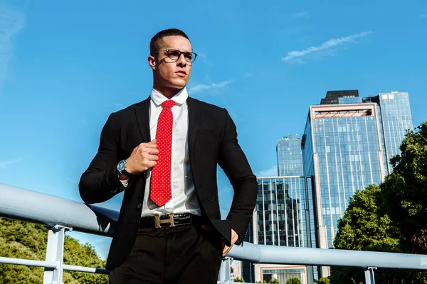 Man dressed in a black suit, red tie, a handsome, sexy, middle age businessman standing in the front of a business district. Portrait of Businessman