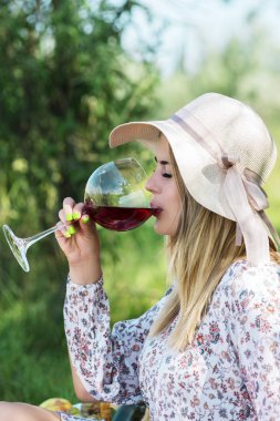 Genç ve güzel kadın kırmızı şarap içiyor. Piknik
