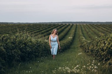 Kafasında çelenk olan güzel ve çekici bir kız gün batımında bir yaz tarlasında yürüyor.
