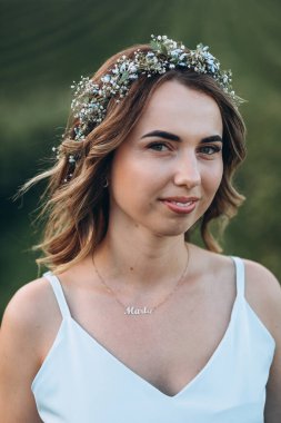 Kafasında çelenk olan güzel ve çekici bir kız gün batımında bir yaz tarlasında yürüyor.