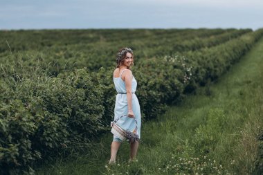 Kafasında çelengi olan güzel bir genç kız bir sepet lavanta ile simetrik bir alanda yürüyor.