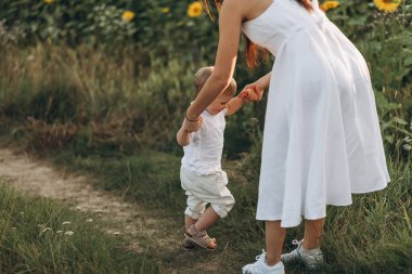 Anne ve oğul ayçiçeği tarlasında sarılır, güler ve oynarlar. Açık havada geçirilen mutlu aile anları. Anneler Günü.