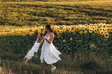 Anne ve oğul ayçiçeği tarlasında sarılır, güler ve oynarlar. Açık havada geçirilen mutlu aile anları. Anneler Günü.