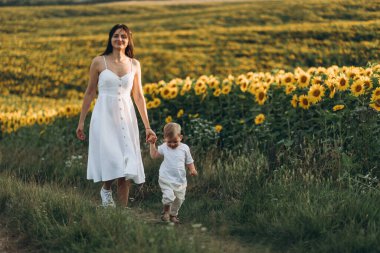 Anne ve oğul ayçiçeği tarlasında sarılır, güler ve oynarlar. Açık havada geçirilen mutlu aile anları. Anneler Günü.