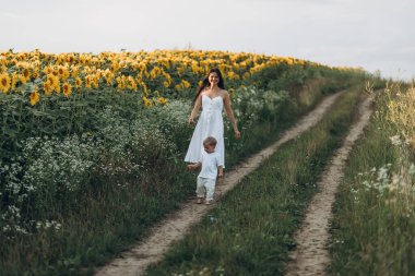 Anne ve oğul ayçiçeği tarlasında sarılır, güler ve oynarlar. Açık havada geçirilen mutlu aile anları. Anneler Günü.