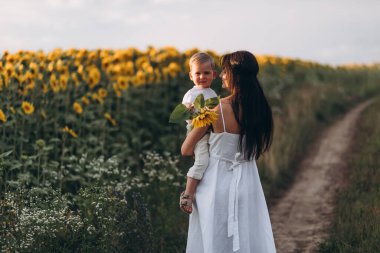 Anne ve oğul ayçiçeği tarlasında sarılır, güler ve oynarlar. Açık havada geçirilen mutlu aile anları. Anneler Günü.