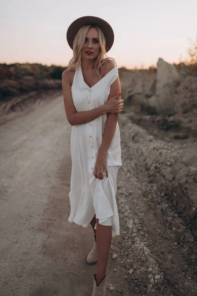 Mulher Loira Bonita Chapéu Vestido Branco Caminha Uma Estrada Deserta — Fotografia de Stock