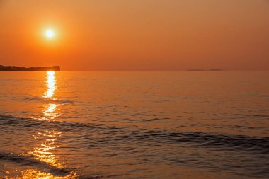 Bir uçurumun bir turuncu günbatımı çerçevede silüeti. Dalgalar deniz buzlu kır. Günbatımı Corfu Island, Yunanistan