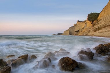 Uzun pozlama Denizi ve kayalar, denize, sahilde günbatımı sırasında dalga günbatımı. Güzel alacakaranlık arka plan. Ünlü Logas beach cliff Corfu Island, Yunanistan