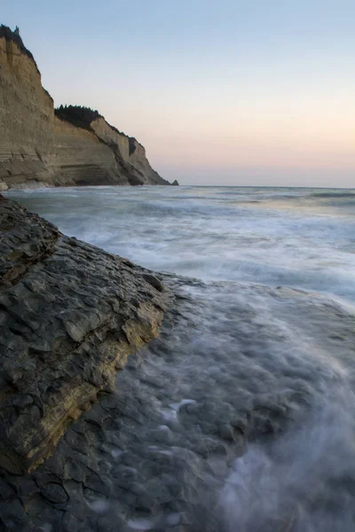 海と岩 ビーチで日没時に波に沈む夕日の長時間露光 美しい夕暮れの背景 コルフ島 ギリシャで有名な Logas の絶壁 — ストック写真