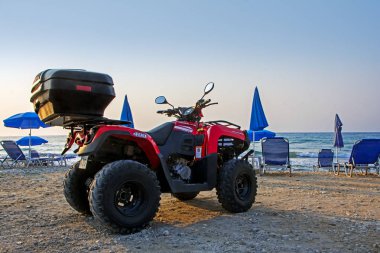 Corfu Island, Yunanistan - 28 Ağustos 2017: Kırmızı siyah zemin üzerine mavi şemsiye, şezlong ve deniz kum plajındaki Atv (arazi aracı) park etmiş. Sahilde Deniz arka plan karşı dört araç
