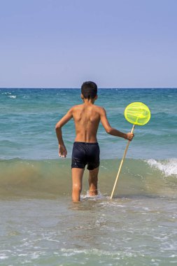 Balık yakalamak için masmavi deniz donanma yüzme şort parlak sarı balık tutma-net ile esmer çocuk giriyor