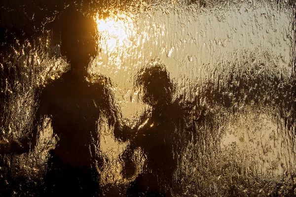 それの下の水の流れと濡れた窓からすを通して 人のうれしそうな子供の抽象的なシルエットが見えます 抽象的なテクスチャで夕暮れ時の人間の体に神秘的な背景 — ストック写真