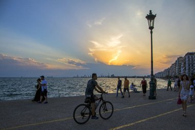 Thessaloniki, Yunanistan - 06 Temmuz 2018: şehir sahil güzel günbatımı arka plan üzerinde yürüyen insanlar. Bisikletçi bisiklet yolu rides