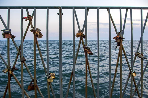 The promise of eternal love symbolized by the closure of a lock on the coast in Thessaloniki, Greece. Rusty padlocks on a metal railing with blue sea background