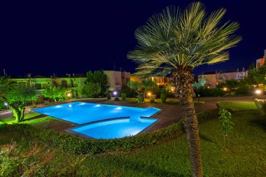 Chalkidiki, Yunanistan - 08 Temmuz 2018: Güzel gece sahne lüks evler ve Halkidikya, Yunanistan için yeşil ağaçlar arasında ışıklı mavi yüzme havuzlu