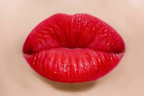 Human kiss lips with glamorous glossy red lipstick on the face of an attractive beautiful woman as a beauty and health concept pertaining to cosmetics and female business fashion
