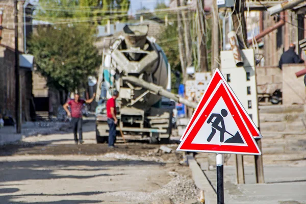 A sign of the road that shows that the road is in repair and workers are working on the street. Concrete mixer truck and workers are on blurred background. Gyumri, Armenia