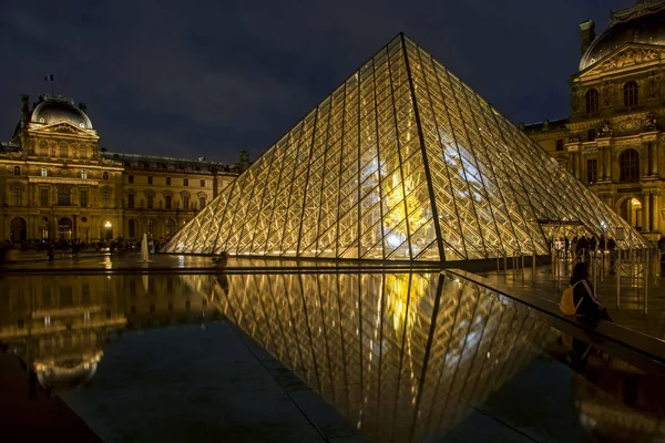 The Louvre museum and illuminated Louvre Pyramid at night reflected in a pond in Paris, France. The Louvre is one of the largest museums in the world and one of the major tourist attractions of Paris