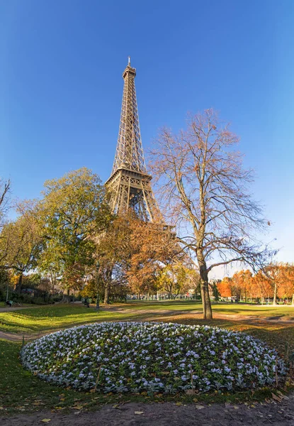 Ultra wide angle vertical panorama of Eiffel Tower over blue sky in Paris, France with round flowerbed on foreground