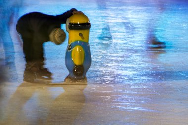 Erivan, Ermenistan - 06 Ocak 2019: Soyut bulanık sahne, insan paten buz pateni pisti gece şehrin üzerinde. Büyük plastik Minion yardımı ile kaymak öğrenme bir çocuk