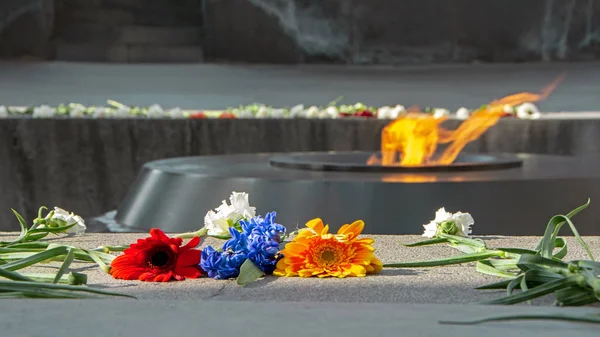 Kırmızı, arka planda Tsitsernakaberd Anıt anıt Ermeni Soykırımı, Erivan, Ermenistan üzerinde bayraklarında sonsuz alev ile Ermeni bayrağı mavi ve turuncu çiçekler bulanık